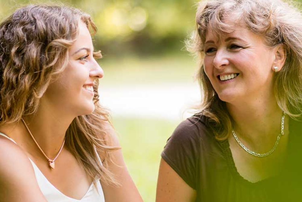 Alumni mother and daughter smile at each other.