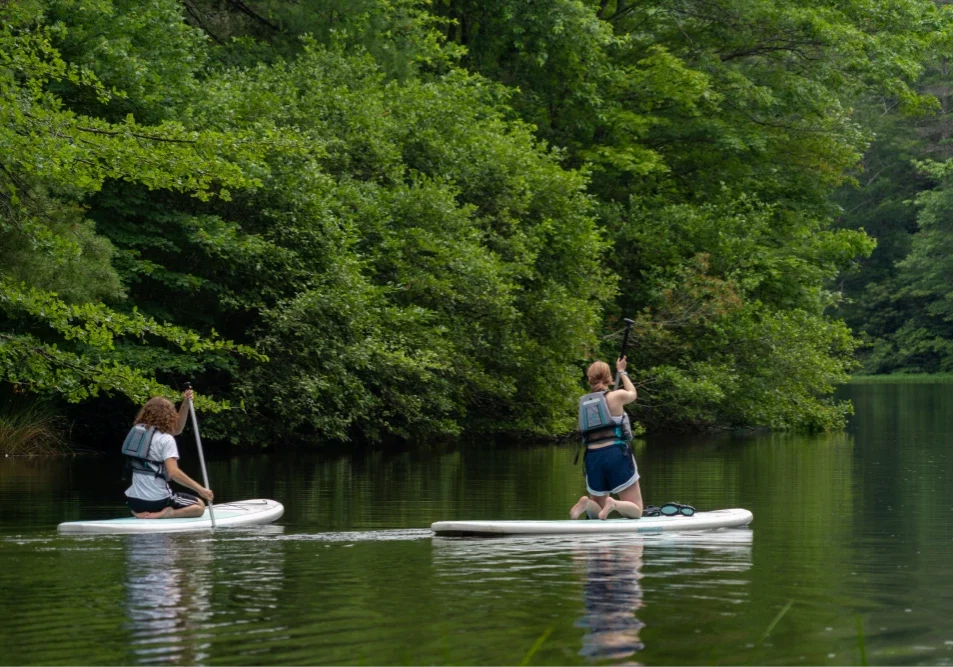 Two students on paddleboards, navigating the peaceful waters of a lake, demonstrating therapeutic outdoor activities.