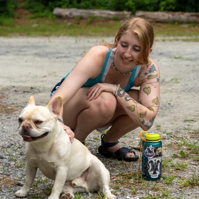 A student crouching and petting a French Bulldog, smiling and enjoying a moment of animal therapy on campus grounds.